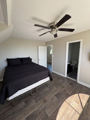 A bedroom with a bed, a ceiling fan, a door leading to a bathroom, and a view of the outside. - Spacious 4-bedroom house with AC in welcoming Santee. Your Home Away from Home! (Santee)