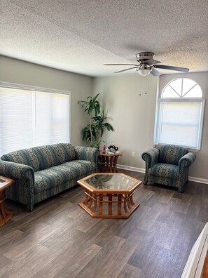 A living room with a sofa, armchair, glass coffee table, and a ceiling fan. - Spacious 4-bedroom house with AC in welcoming Santee. Your Home Away from Home! (Santee)
