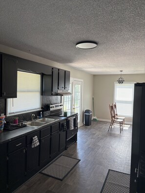 A modern kitchen with dark cabinetry, a stainless steel sink, and a built-in oven. - Spacious 4-bedroom house with AC in welcoming Santee. Your Home Away from Home! (Santee)
