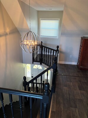 A staircase with a chandelier, wooden railing, and a view of a door and window. - Spacious 4-bedroom house with AC in welcoming Santee. Your Home Away from Home! (Santee)