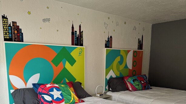 Ein Hotelzimmer mit zwei Betten, weißer Bettwäsche, farbenfroher Wandkunst und einem Stadtblick-Motiv.