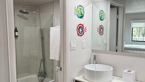 Ein modernes Badezimmer mit einer gläsernen Dusche, einer weißen Toilette, einem weißen Waschbecken und einem Spiegel mit dekorativen Aufklebern.