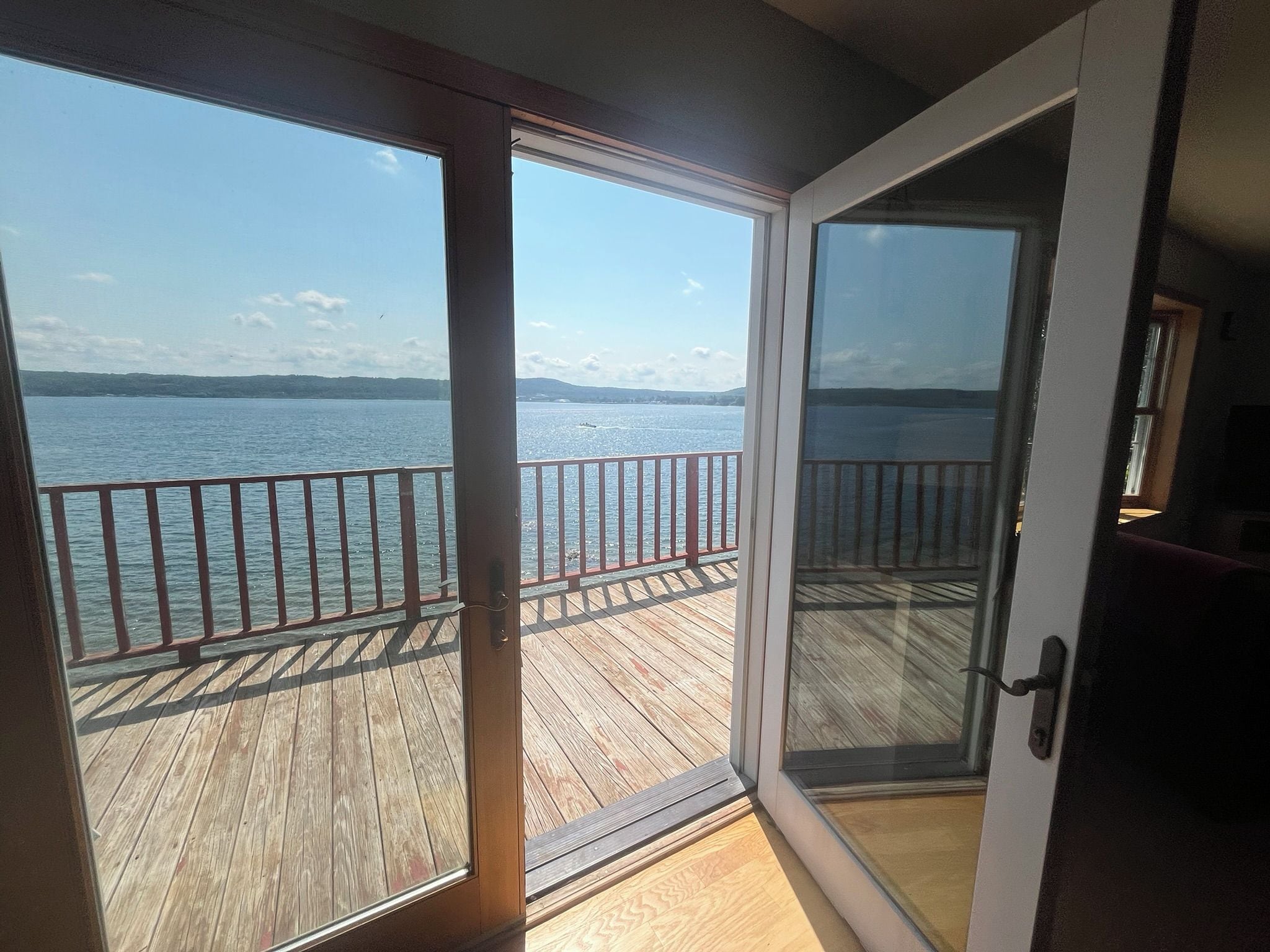 A room with a sliding glass door leading to a wooden deck overlooking a body of water.