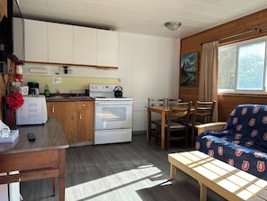 A compact kitchen with a stove, oven, and sink, wooden cabinets, and a dining area with a table and chairs.
