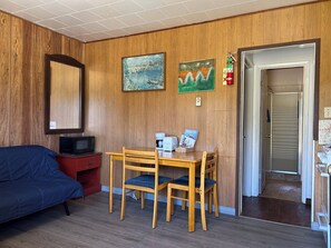 A room with a wooden paneled wall, a bed, a table with chairs, a television, and a door leading to another room.