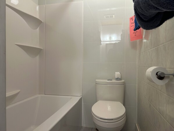 A bathroom with a white bathtub, toilet, and tiled walls.