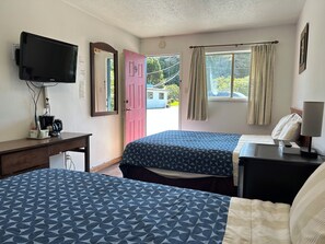 Habitación de hotel con dos camas, un escritorio con cafetera, televisión y ventana con cortinas.