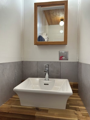 Un baño con un lavamanos blanco, un espejo con marco de madera y una lámpara en el techo.
