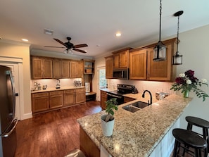 A kitchen with wooden cabinets, granite countertops, a stainless steel refrigerator, and a ceiling fan.