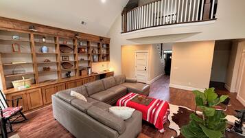 Amplia sala de estar con sofá seccional, estanterías de madera y una escalera que conduce a un nivel superior.