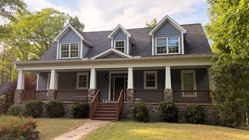 A two-story house with a covered porch, stone foundation, and a stone staircase leading to the front door.