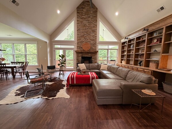 A spacious living room with a stone fireplace, a large sectional sofa, and a dining area with a wooden table and chairs.