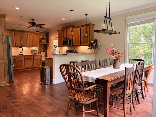 A spacious kitchen with wooden cabinets, a dining area with a large table and chairs, and a view through a window.