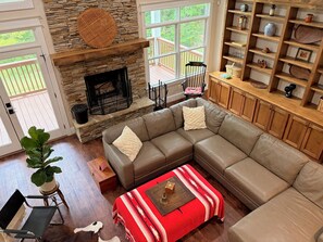 A living room with a stone fireplace, a sectional sofa, a coffee table, and a bookshelf.