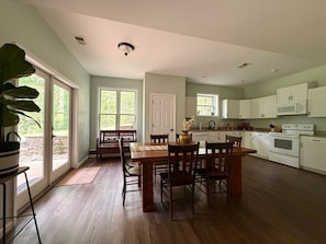 A spacious kitchen with white cabinets, a dining area with a wooden table and chairs, and a large window providing natural light.
