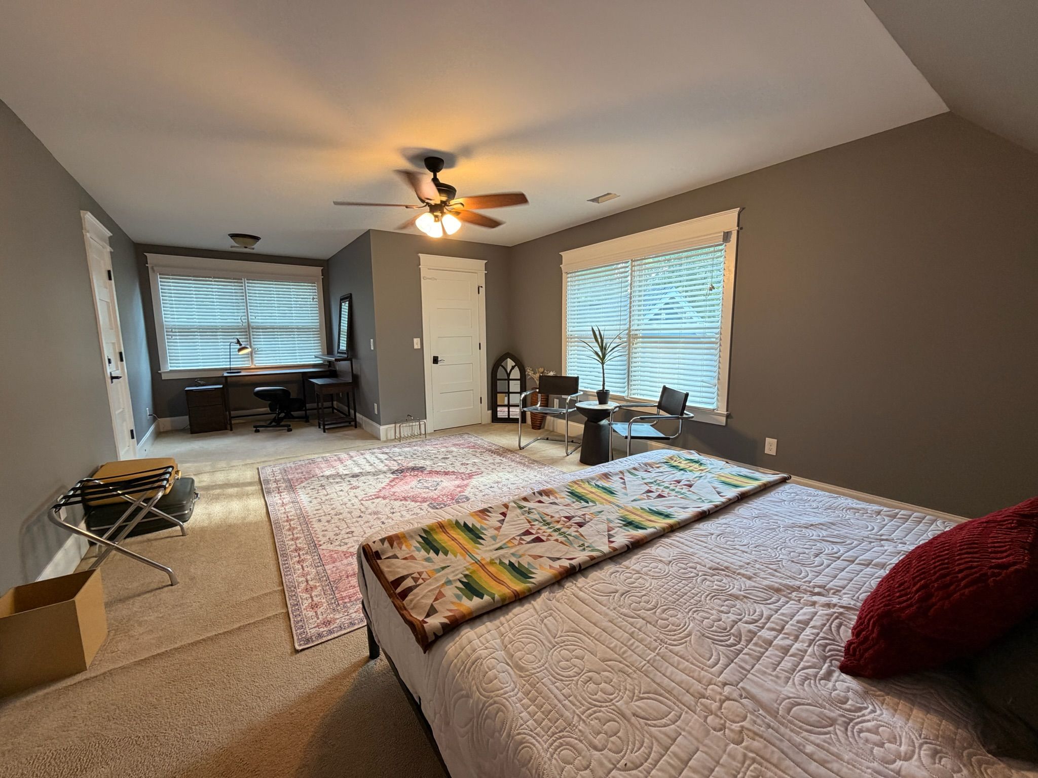 A bedroom with a bed, a desk, a chair, and a ceiling fan.