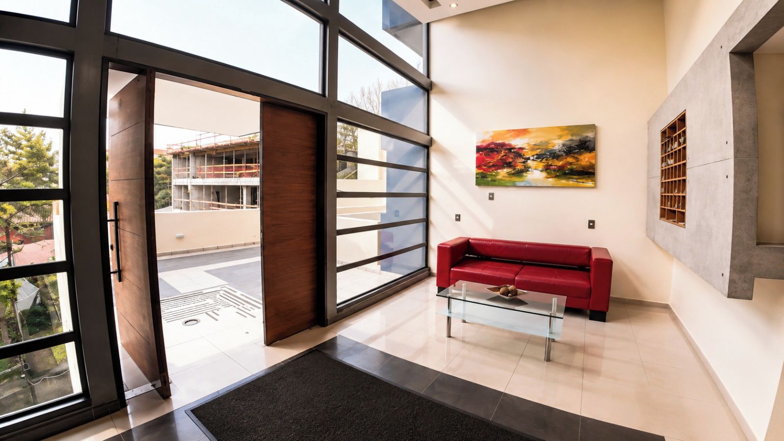 Un hall d’entrée moderne avec un canapé rouge, une table basse en verre et un tableau accroché au mur.