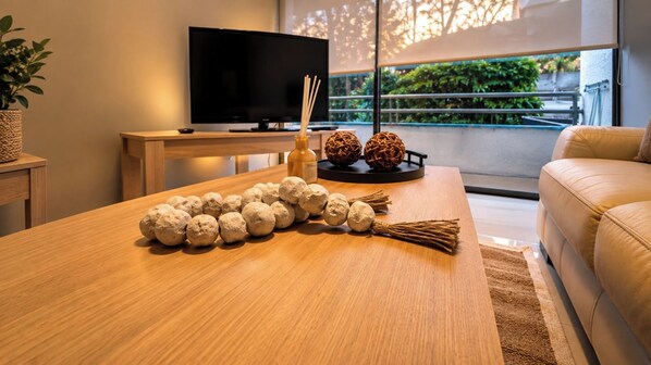 Ein modernes Wohnzimmer mit einem Couchtisch aus Holz, einem Flachbildfernseher und Blick ins Grüne.