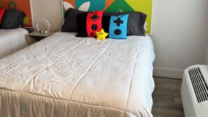 Ein Hotelzimmer mit zwei Betten, einem großen, farbenfrohen Kunstwerk an der Wand, einem Nachttisch mit einer Uhr und einer weißen Klimaanlage.