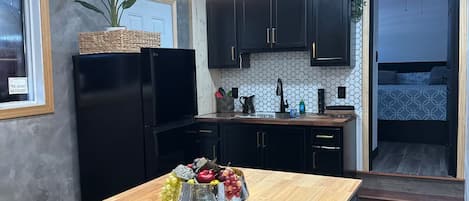 A modern kitchen with a central island, black cabinets, a built-in oven, and a hanging light fixture.