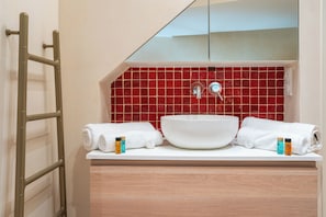 A bathroom with a white sink, red tiled backsplash, and a wooden vanity. - Le Charme Chavannes - Welkeys (Paris)