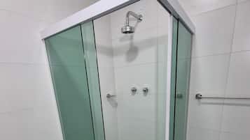 A glass-enclosed shower stall with a white tiled floor and a metal handrail.