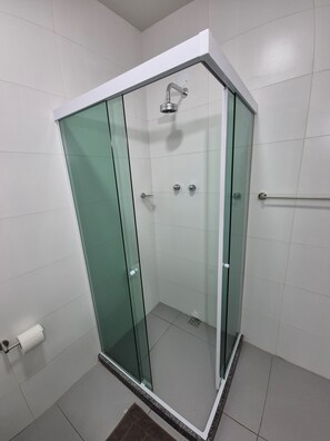 A glass-enclosed shower stall with a white tiled floor and a metal handrail.