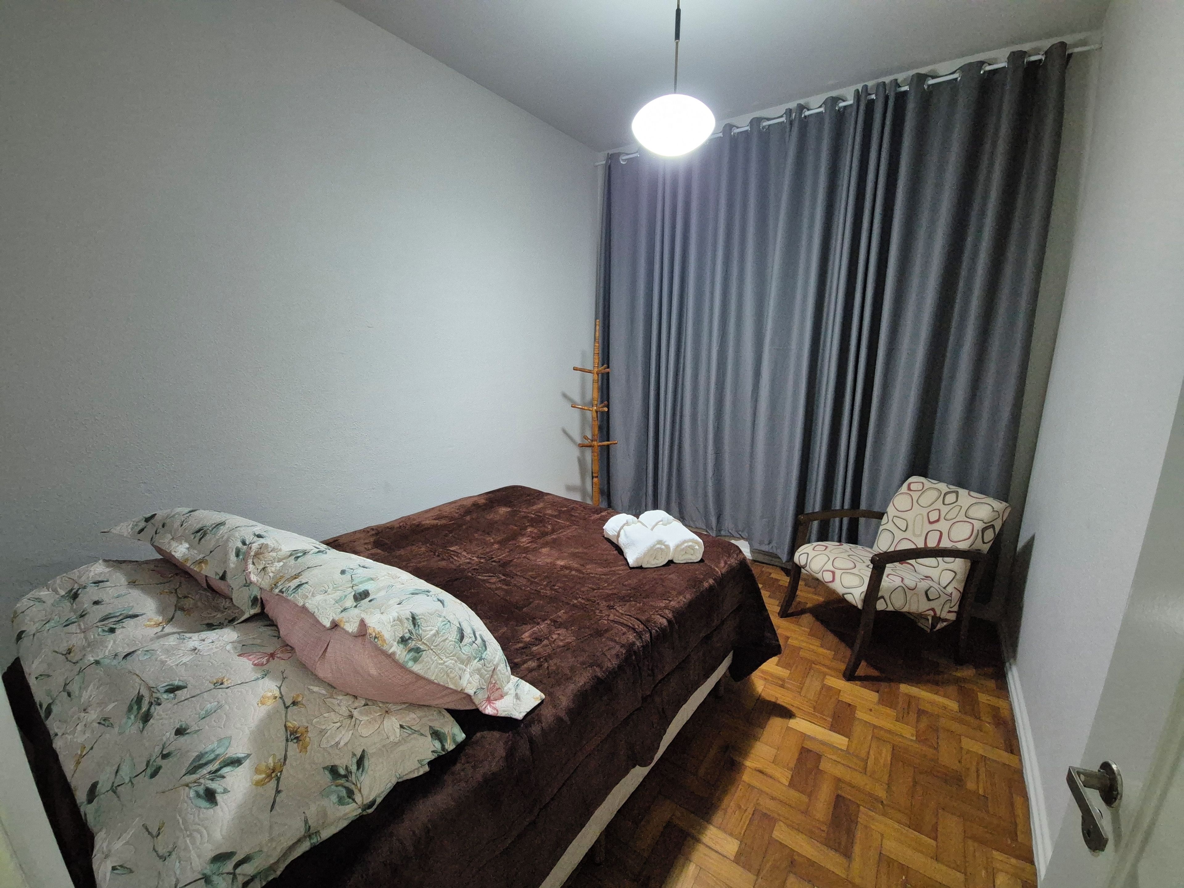 A bedroom with a bed, a chair, a hanging light, and a curtain.