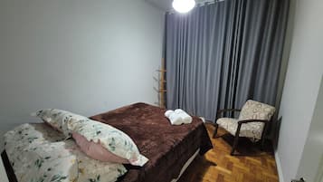 A bedroom with a bed, a chair, a hanging light, and a curtain.