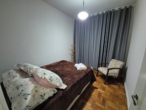 A bedroom with a bed, a chair, a hanging light, and a curtain.