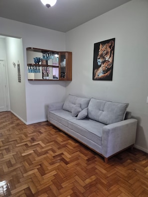 A living room with a grey sofa, wooden herringbone flooring, a glass cabinet with decorative items, and a painting of a lion.