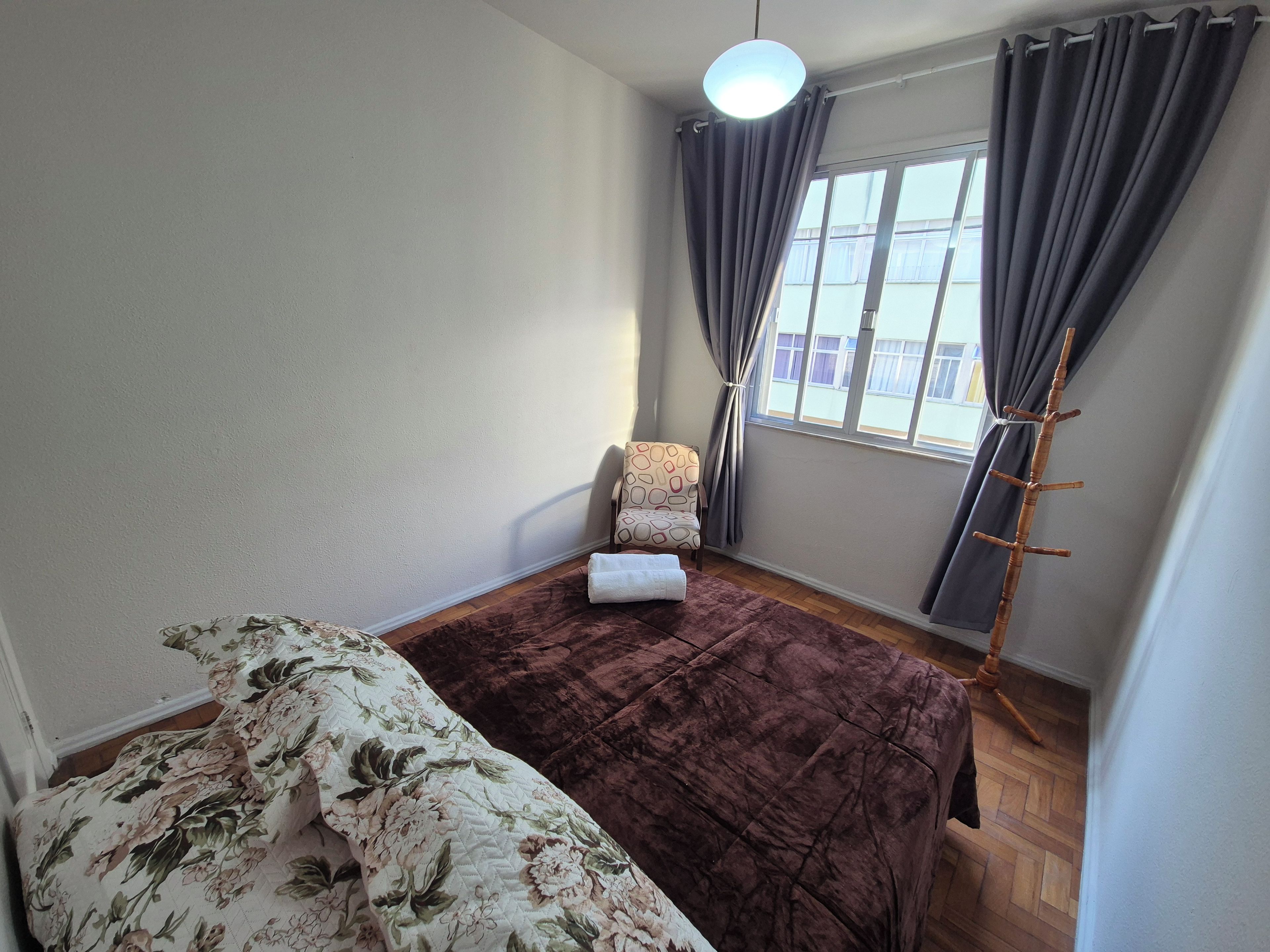A room with a bed, a chair, a window with curtains, and a coat rack.