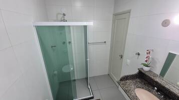 A bathroom with a glass-enclosed shower, a sink with a granite countertop, and a potted orchid.