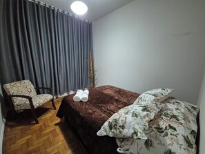 A room with a bed, a chair, a wooden floor, and a curtain.