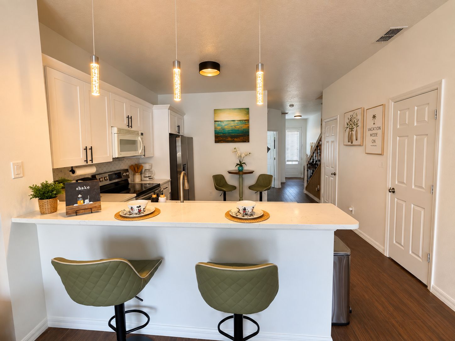 A modern kitchen with a central island, pendant lighting, and a view into the dining area.