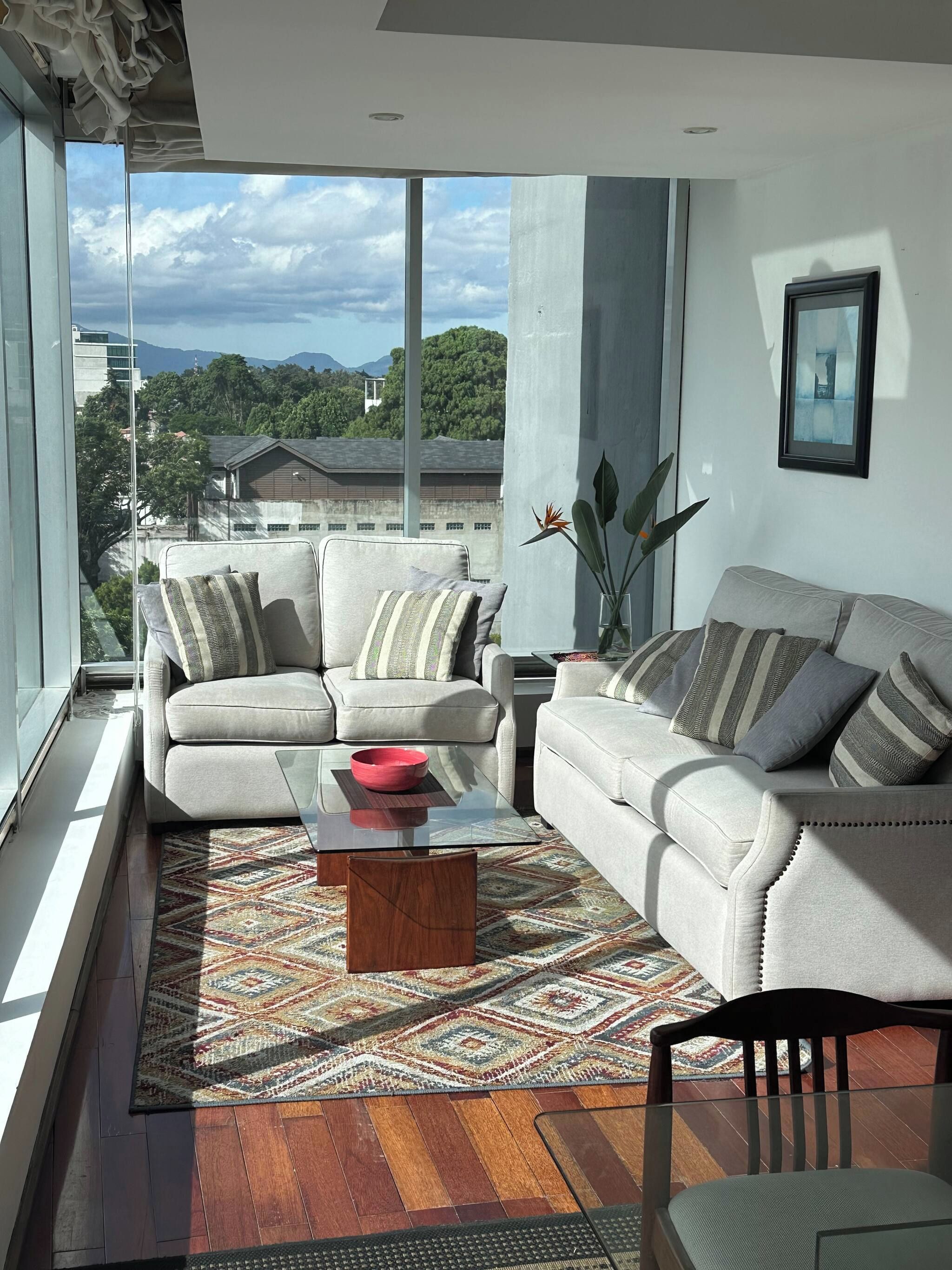 Ein modernes Wohnzimmer mit einer Sofagarnitur, einem Couchtisch und Blick auf eine Stadtlandschaft durch große Fenster.