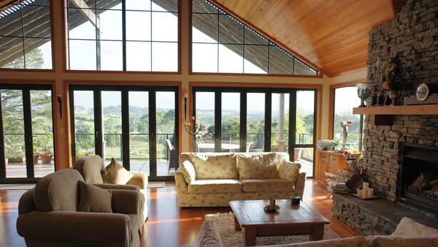 A spacious living room with large windows, a stone fireplace, and a cozy seating area. - O'Grady Lodge - The Whole Wing (Wainui)