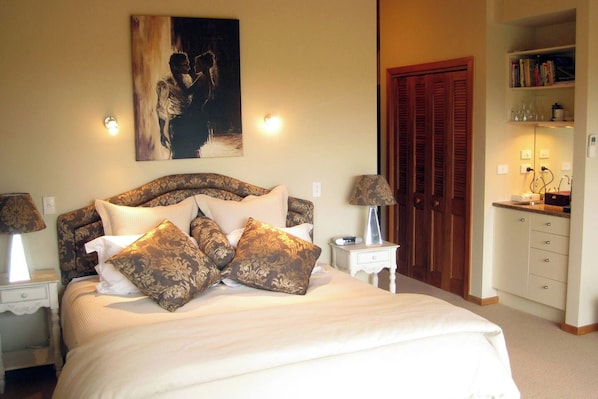 A bedroom with a large bed, two bedside tables with lamps, a wooden door, and a bookshelf.