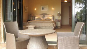 A hotel room with a bed, a nightstand, a lamp, and a dining area with wicker furniture. - O'Grady Lodge - The Whole Wing (Wainui)