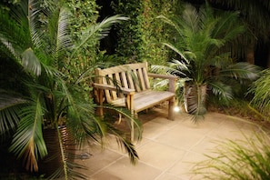 A wooden bench in a garden with potted palm plants and a tiled floor.