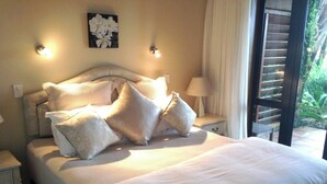 A bed with multiple pillows, a nightstand, a wall-mounted light, and a window with blinds. - O'Grady Lodge - The Whole Wing (Wainui)