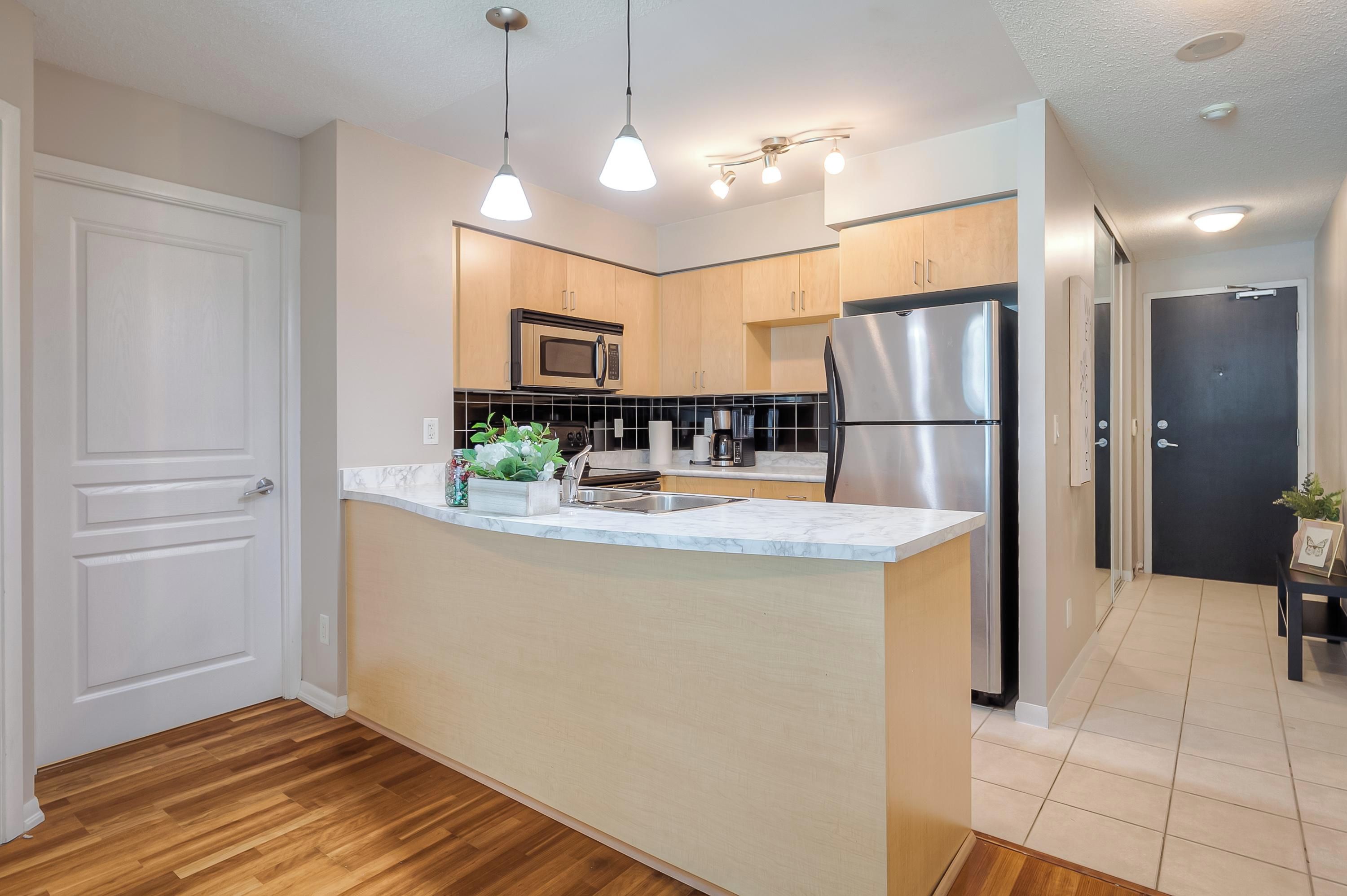 A modern kitchen with a central island, stainless steel appliances, pendant lighting, and wooden cabinetry.