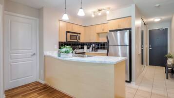 A modern kitchen with a central island, stainless steel appliances, pendant lighting, and wooden cabinetry.