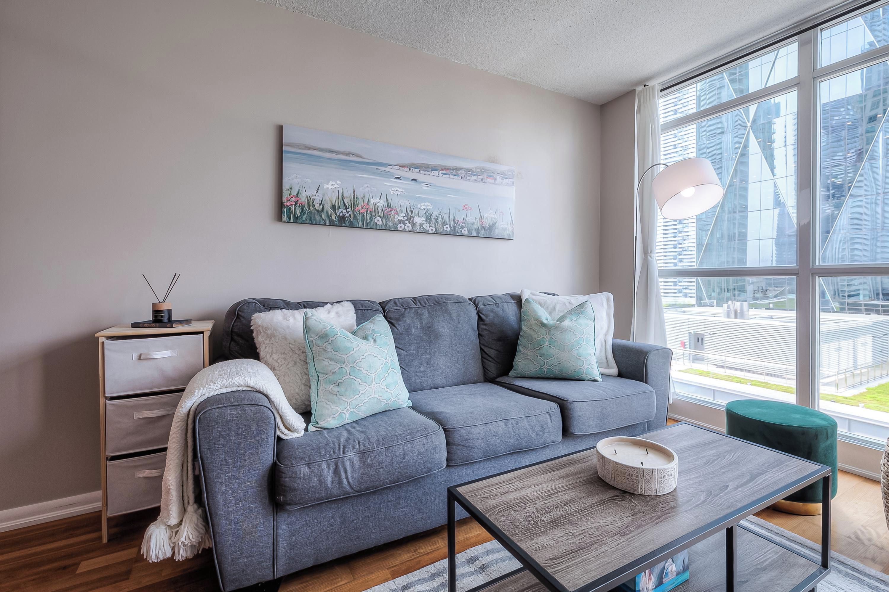 A modern living room with a grey sofa, a side table, a coffee table, and a large window with a city view.