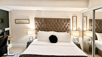 A hotel room with a large bed, two bedside tables with lamps, a desk with a chair, and a large mirror.