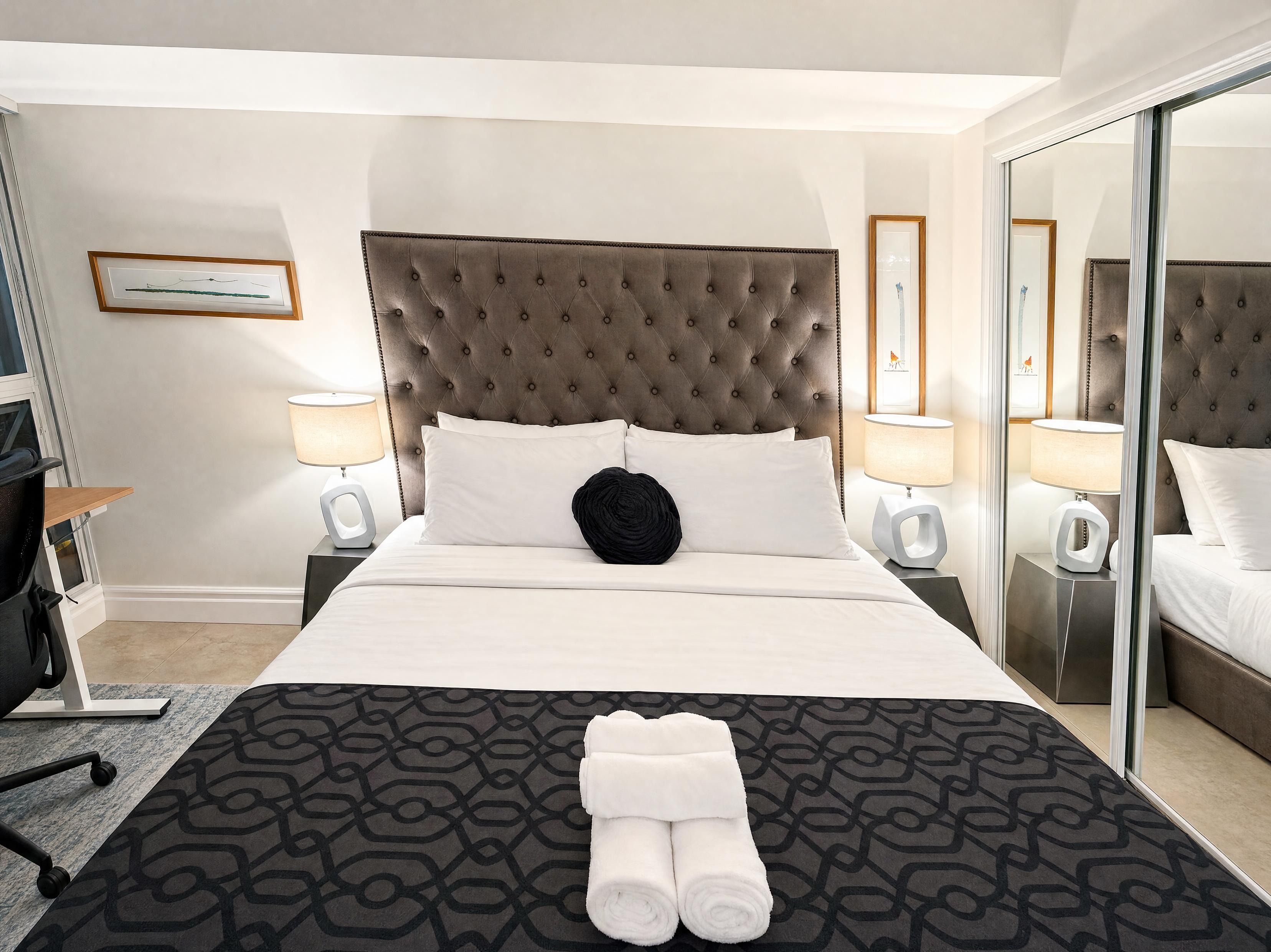 Een hotelkamer met een groot bed, twee nachtkastjes met lampen, een spiegel en een kamerkleed met patroon.