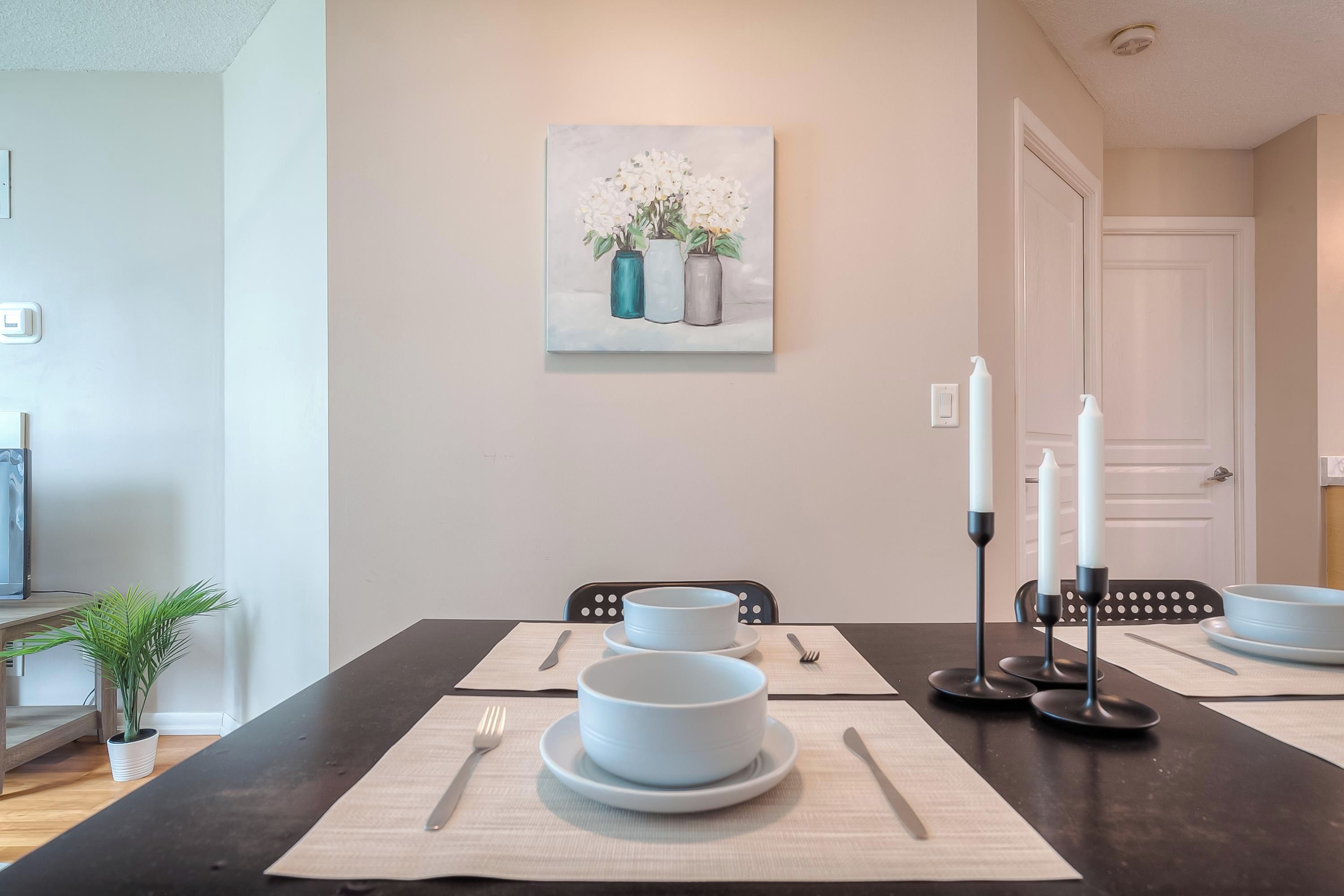 A dining area with a table set for four, a painting above the table, and a door in the background.