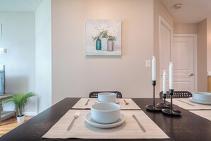 A dining area with a table set for four, a painting above the table, and a door in the background. - South Core Suites (Toronto)