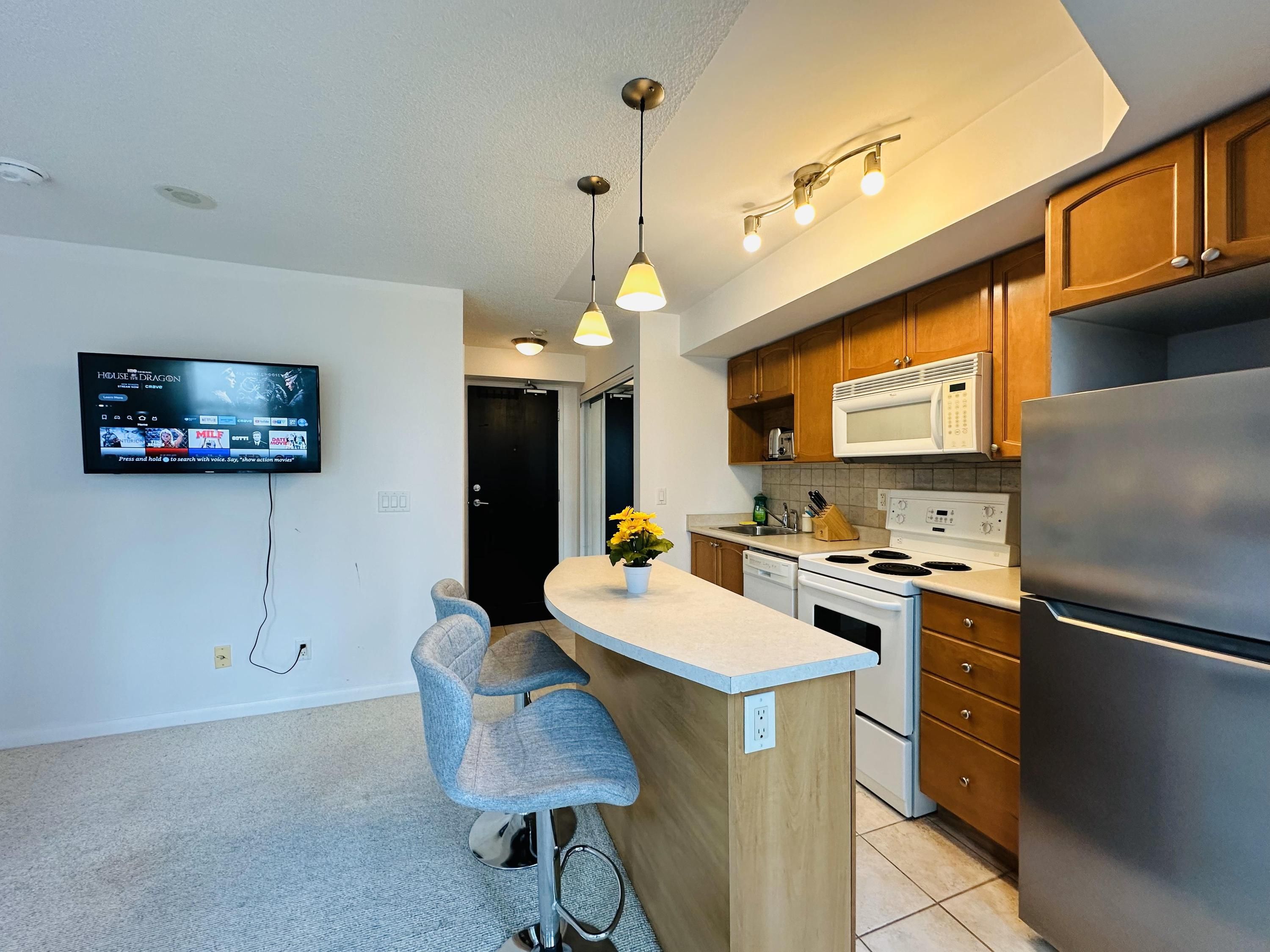 A modern kitchen with a built-in microwave, stainless steel refrigerator, and a flat-screen TV mounted on the wall.