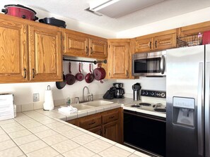 A kitchen with wooden cabinets, a stainless steel refrigerator, a microwave, a stove, and hanging pots. - Cozy Resort Condo, Family Friendly Pools (St. George)